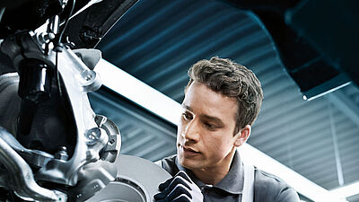 Kraftfahrzeugmechatroniker bei der Tätigkeit am Bremssystem eines BMW